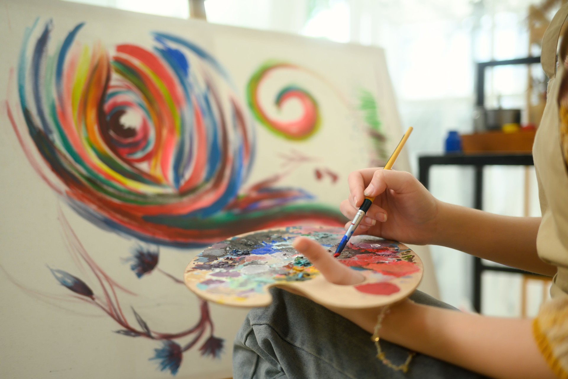 Close up of female artist mixing paint on a palette while working on her painting in studio